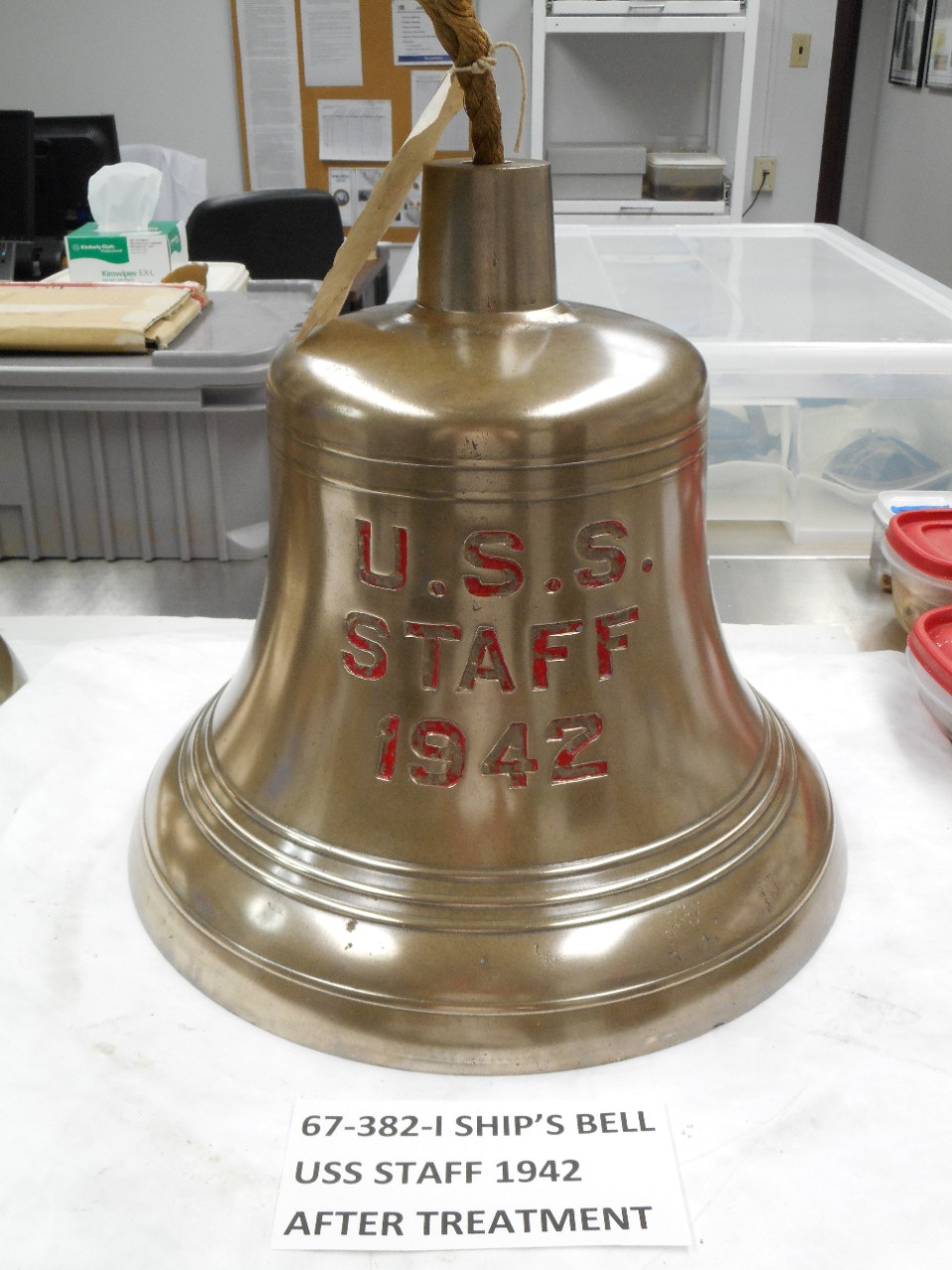 Ship's bell from USS Staff. Bell is shiny brass with stamped letters "U.S.S. / Staff / 1942." Red paint in the letters.