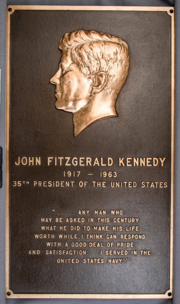 Memorial plaque for John F. Kennedy from USS John F. Kennedy (CV-67). One brass memorial plaque from the aircraft carrier USS John F. Kennedy (CV/CVA-67) The plaque is rectangular in shape. At the top is a raised profile bust of John F. Kennedy, ...