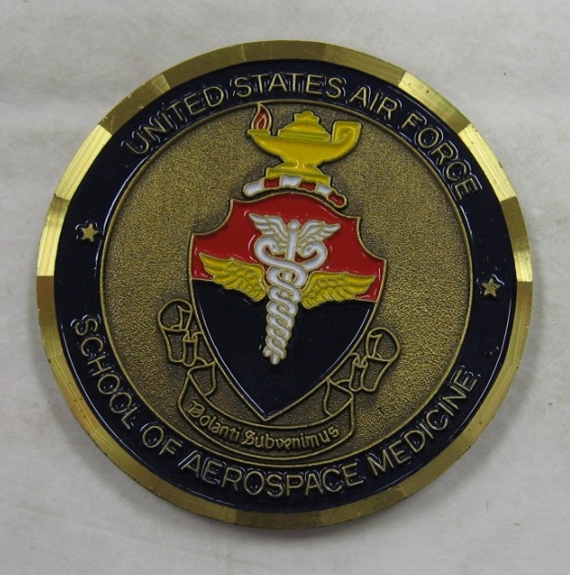 This commemorative Medallion from the United States Air Force School of Aerospace Medicine is a circular medallion with central shield device containing medical symbol with yellow oil lamp burning above shield. Inscription around image reads "Uni...