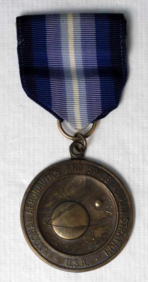 <p>One Type I NASA&nbsp;Distinguished Service Medal. Medal is sterling silver. Planchet is the official Seal of NASA with &quot;National Aeronautics and Space Administration/USA&quot; around the rim. The reverse is oak branches around the rim with &quot;Exceptional Service&quot; in raised letters. The planchet is attached with a suspension ring to a tapered ribbon. The colors of the ribbon are&nbsp;Navy blue, blue, purple, sky blue, and white. The pin and clasp is sewn to the ribbon.</p>
