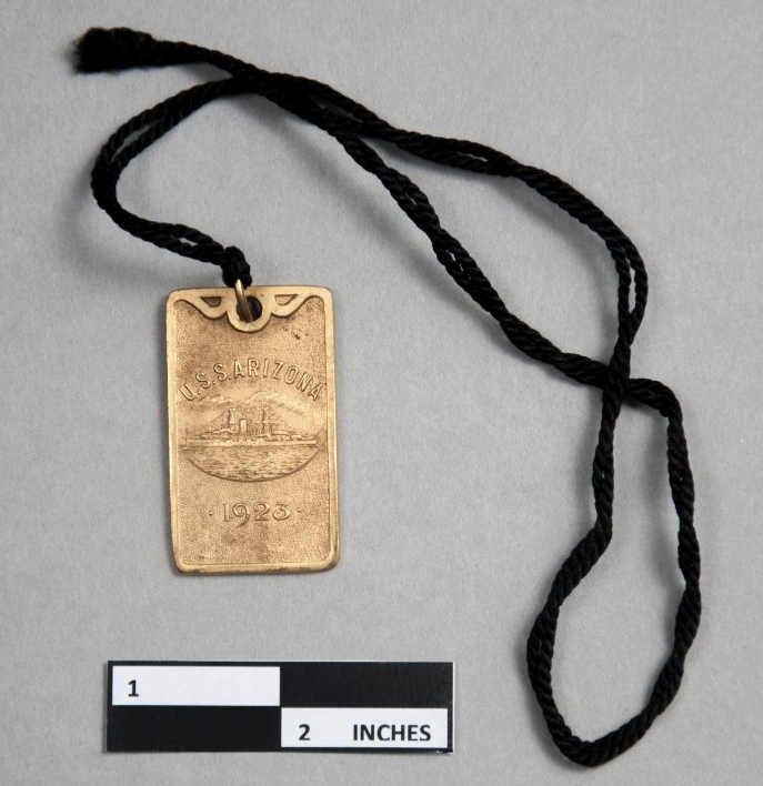 <p>Rectangular brass pendant with relief depiction of USS Arizona. Pendant embossed above image &quot;U.S.S. Arizona&quot; and below image 1923.&nbsp;</p>
