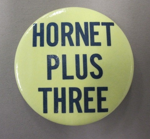 <p>One circular yellow metal button with a pin clasp on the reverse side and&nbsp;dark blue&nbsp;lettering on the obverse side that reads&nbsp; &quot;Hornet / Plus / Three.&quot;</p>

