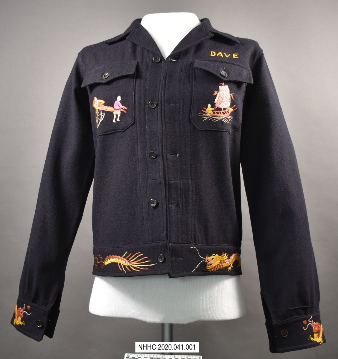 The front of the blue wool cruise jacket with colorful embroidery on the front breast pockets. The right breast pocket is embroidered with a rickshaw. The left breast pocket is embroidered with a Chinese junk and the name Dave embroidered above i...
