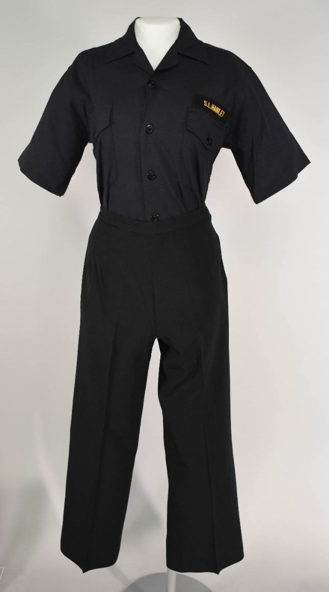 One female Midshipman Working Uniform Blue A. Uniform consists of a pair of dark blue trousers and a dark blue shirt sleeve shirt. The trousers have three buttons and one zipper fly on the proper left hip. The shirt has five black plastic buttons...