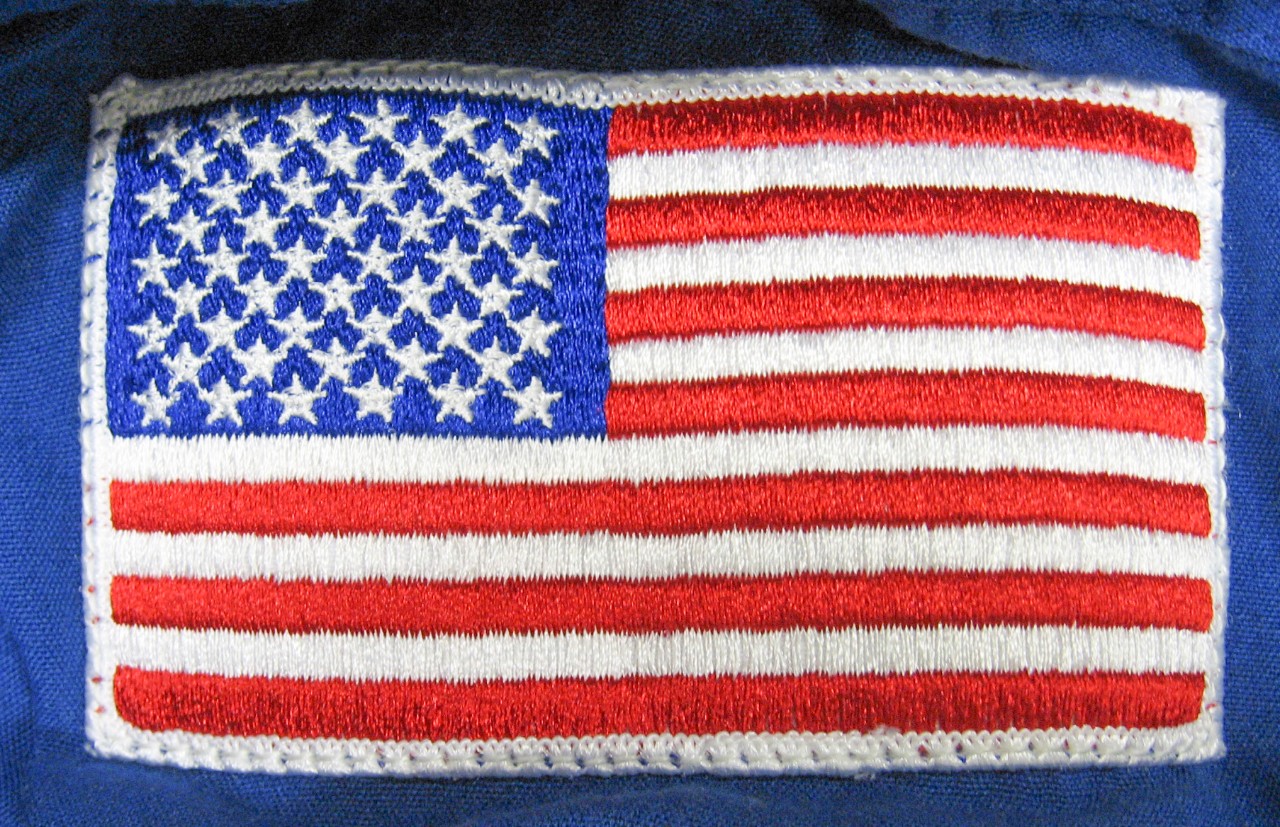 American flag patch on left shoulder of NASA coveralls.