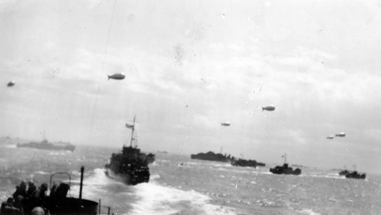 Collection of 36 photos related to the US Navy career of John Robert Hoblit, including imagery associated with D-Day. The photographs are noted to have been taken on June 6, 1944 (D-Day) and include USS Augusta (CA-31) at sea off the coast of France amongst several unidentified ships; USS LCI(L)-540; LCI(L)-542 (including shore landing); troop landings off invasion beaches; as well as various unidentified landing craft with barrage balloons overhead. The remaining images generally consists of photos related to Hoblit and his fellow sailors aboard ship and on shore (likely at boot camp), 1943-1944. Additional materials donated to NHHC (library and museum) suggest Hoblit served aboard LCI(L)-542. It is unknown if he took the D-Day photographs himself. 