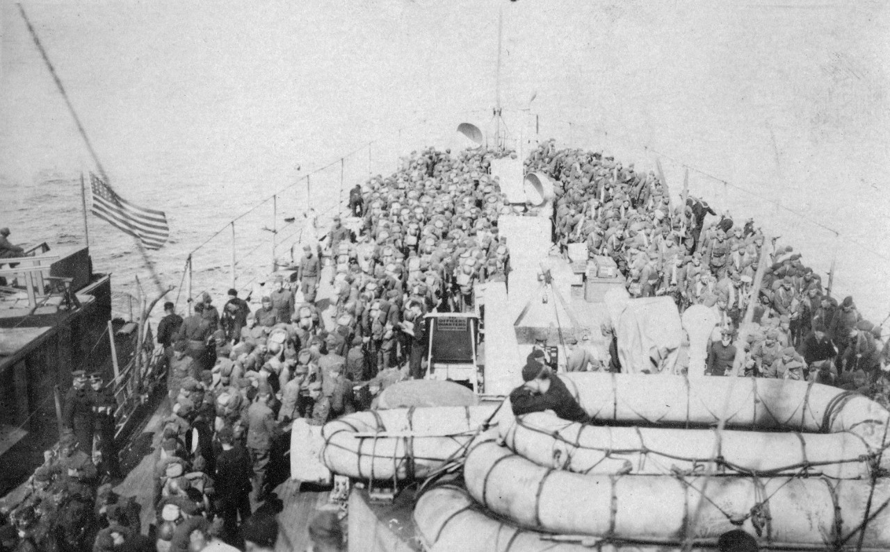 Collection of 76 photographs mostly related to the USS Montana (ACR-13) in late 1918 and first half of 1919. During this time, she made six voyages from France to the United States, bringing 8,000 American troops home from the former WWI combat zone. The photos mainly depict her troop transportation service, though a few were taken during USS Montana’s mid-1919 trip to the Pacific. The collection includes views onboard USS Montana (including the 10-inch gun turret, conning tower and bridge), onboard activities such as baseball pitching practice on the midships’ superstructure, holystoning deck planking, and boxing practice. The bulk of the photographs are scenes showing the transportation of troops from France, specifically musicians giving a concert on the deck, troops on the deck just after boarding at Brest (they are still wearing field packs and rifles, indicating they have just come aboard), troops relaxing on the after deck with a mascot dog, ferry lighter Amackassin bringing troops to USS Montana in Brest Harbor (bridge wings feature her name and initials A.T.S. – for Army Transport Service), and  a welcome boat greening troops in New York Harbor. The photographs showing troop transportation from ferry boats to the USS Montana are all excellent. There are also several images of the ship’s voyage to the US West Coast via the Panama Canal in mid-1919. The Puget Sound Navy Yard is visible in several views. The photographs were purchased and donated by Mark Kulikowski. Item level descriptions of each photograph are available. 