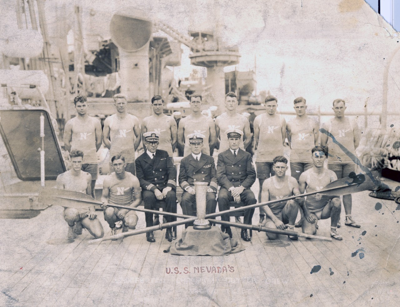 Collection of two photos related to USS Nevada (BB-36) taken in 1923 - one is a starboard broadside view of the ship and the other is the ship's Race Boat Crew (Fleet Champions 1921-1923) (officers identified include: CAPT J.M. Luby and CDR D.A. Scott). Both images are heavily damaged. 