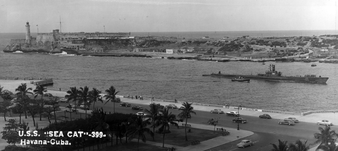 One oversize black and white photo of the submarine USS Sea Cat (SS-399) with crew assembled on deck, passing Morro Castle at the entrance to Havana Harbor, Cuba, circa 1951.