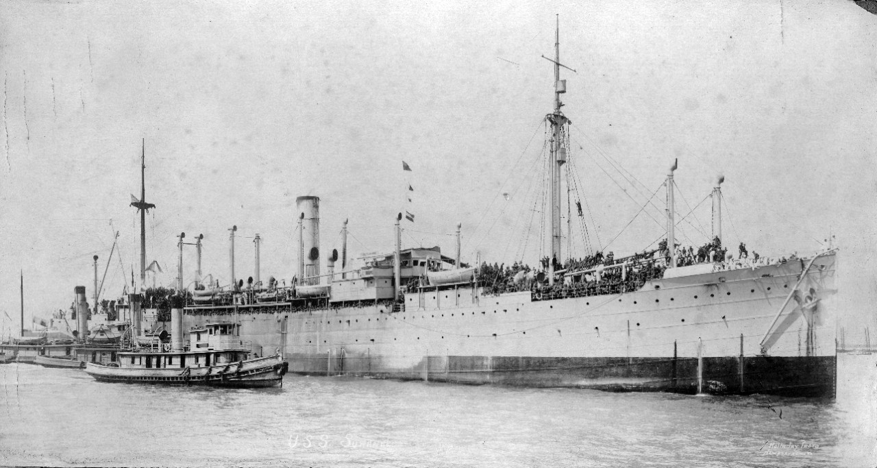 Single oversized photograph of USS Suwanee (ID-1320) circa 1918 as a troop transport following WWI. Several tug boats are seen alongside the ship. 