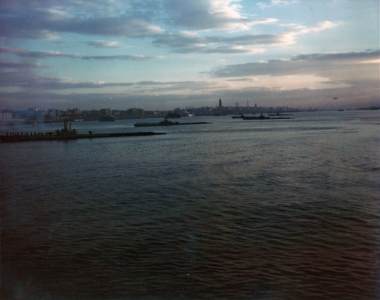 Submarines in the Hudson River, at sunset on Navy Day, just after President Truman steamed by them in USS Renshaw (DD-499). Sub at left is USS Crevalle (SS-291). Tenders in left and center background are USS Howard W. Gilmore (AS-16) and USS Orion (AS-18).