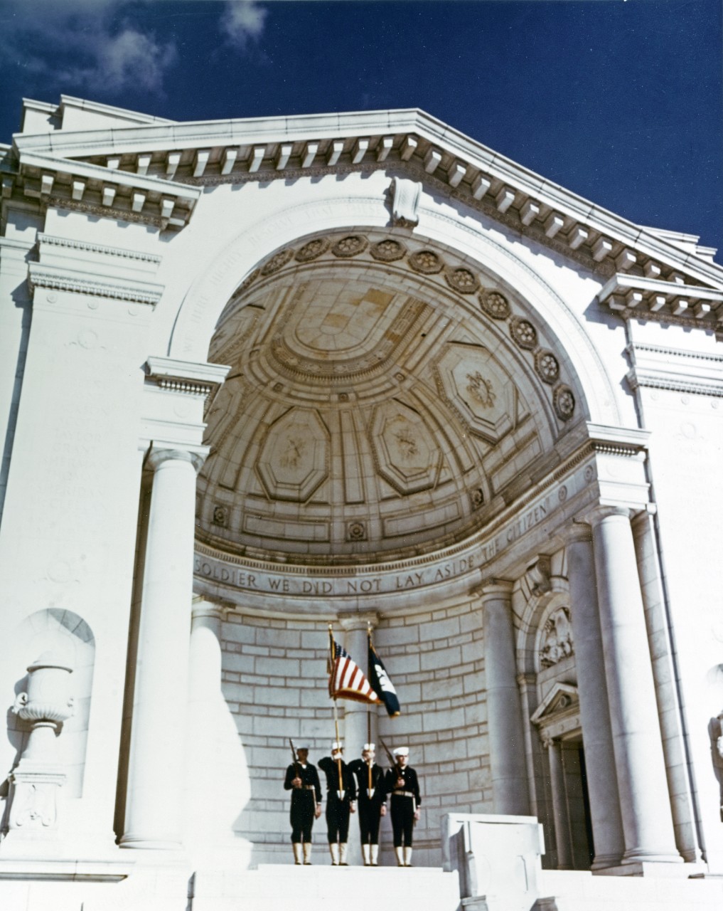 Framed by the columns and arch of the rostrum of the Arlington National Cemetery Amphitheater, a Navy color guard pays tribute to the fighting men who have given their lives for their nation. Photographed during the Second World War.
