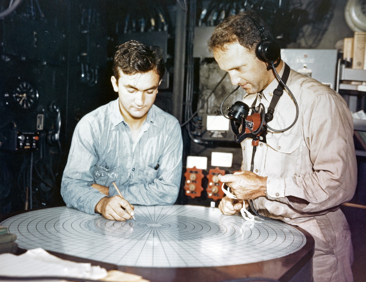 Ship's Executive Officer and a Quartermaster use plotting board to keep track of movements, circa 1944. Headset helps the Exec keep in constant communication with the Captain and the ship's other departments. Photographed prior to late July 1944.