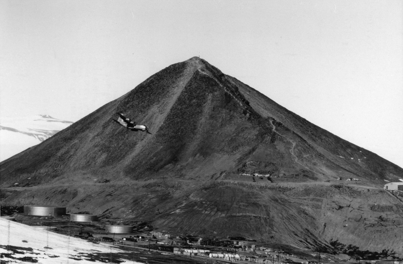 An LC-130F Hercules cargo transport aircraft assigned to Antarctica Development Squadron Six (VXE-6) in flight over McMurdo Station, with Observation Hill in the background