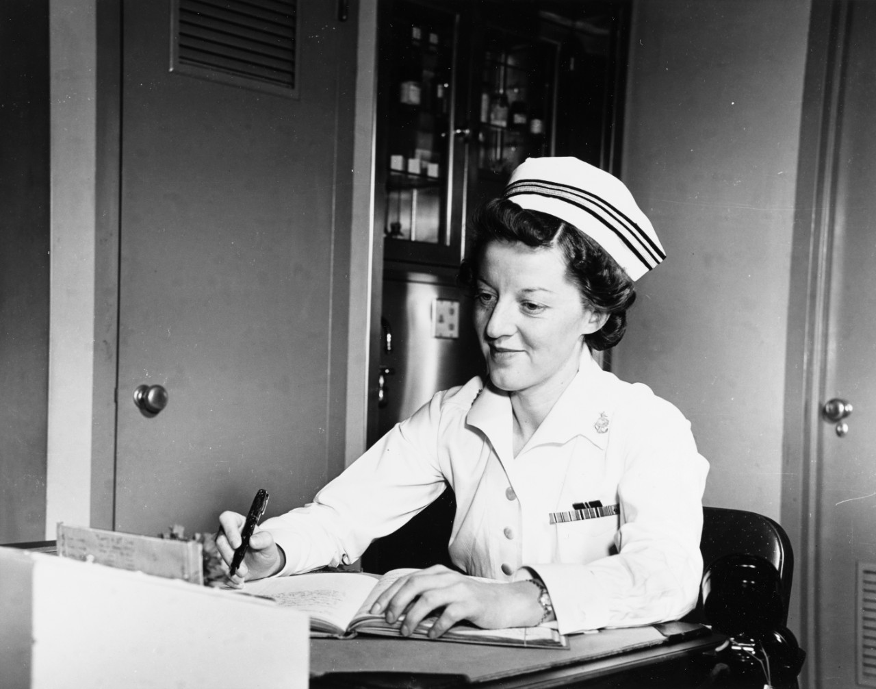 LTJG Ann Bernatitus, seated at a desk at a nurse's station, circa 1943-early 1943.