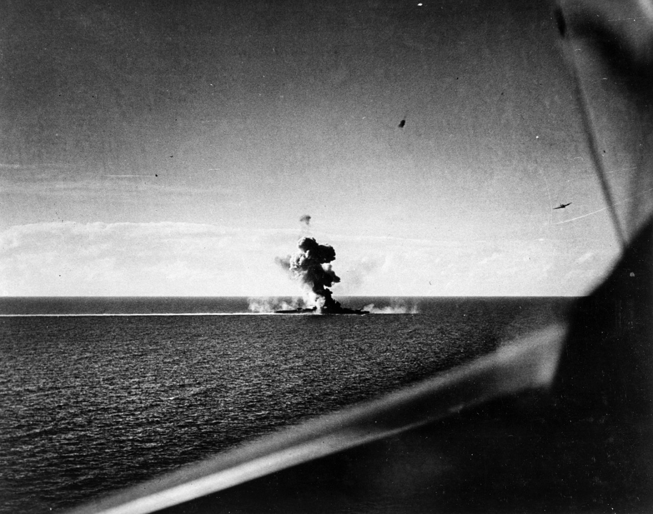 Japanese cruiser Kumano is bombed by planes of Task Force 38 on 26 October 1944, following the Battle off Samar. She had lost her bow the previous day, and was further crippled by this attack, but was not sunk until the following month. Photographed from a USS Hancock plane. Note SB2C Helldiver at right center.