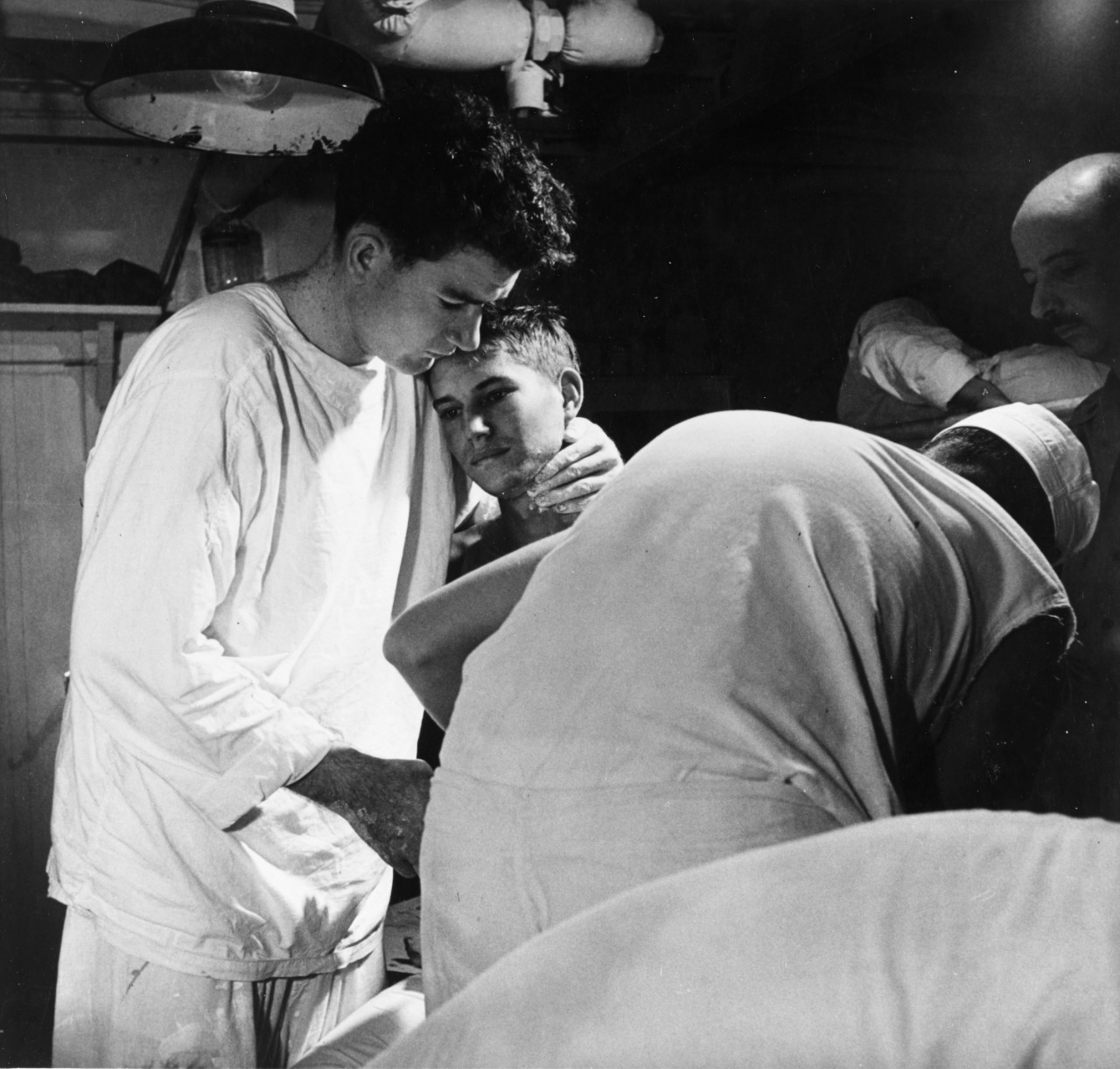 Army Private J.B. Slagle receives his daily dressing of wounds on board USS Solace (AH-5), while en route from Okinawa to Guam, May 1945. A corpsman comforts him during the painful process. Photographed by Lieutenant Victor Jorgenson, USNR.