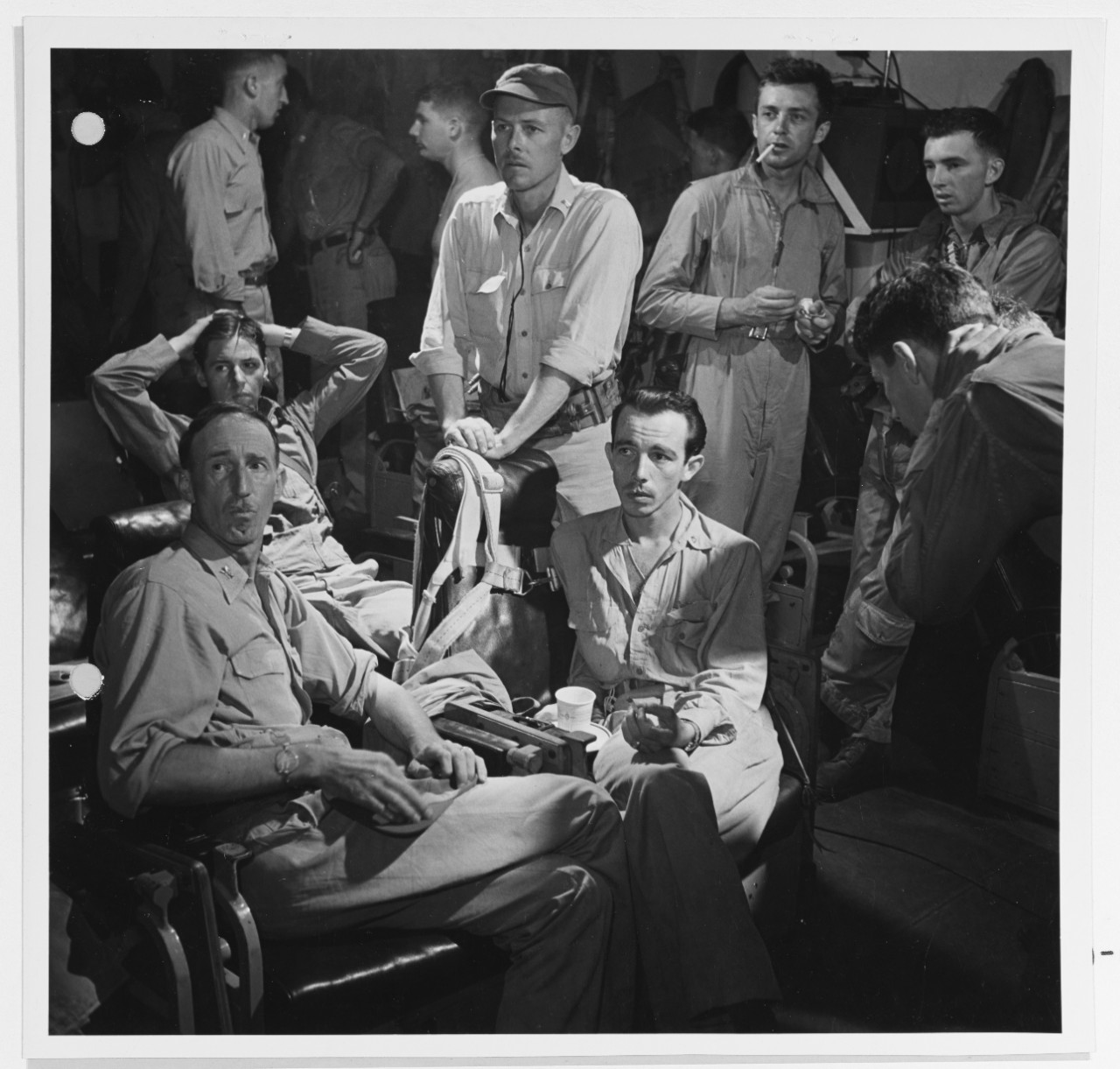 CAPT. Stuart H. Ingersoll (left), C/O of USS Monterey (CVL-26) in the pilots ready room of his ship, listening to intern-plane conversations of bomber pilots during a raid on Tinian, 11 June 1944. With him are fighter pilots, and ship's Air Group Commander, LCDR Roger W. Mehle (seated). 