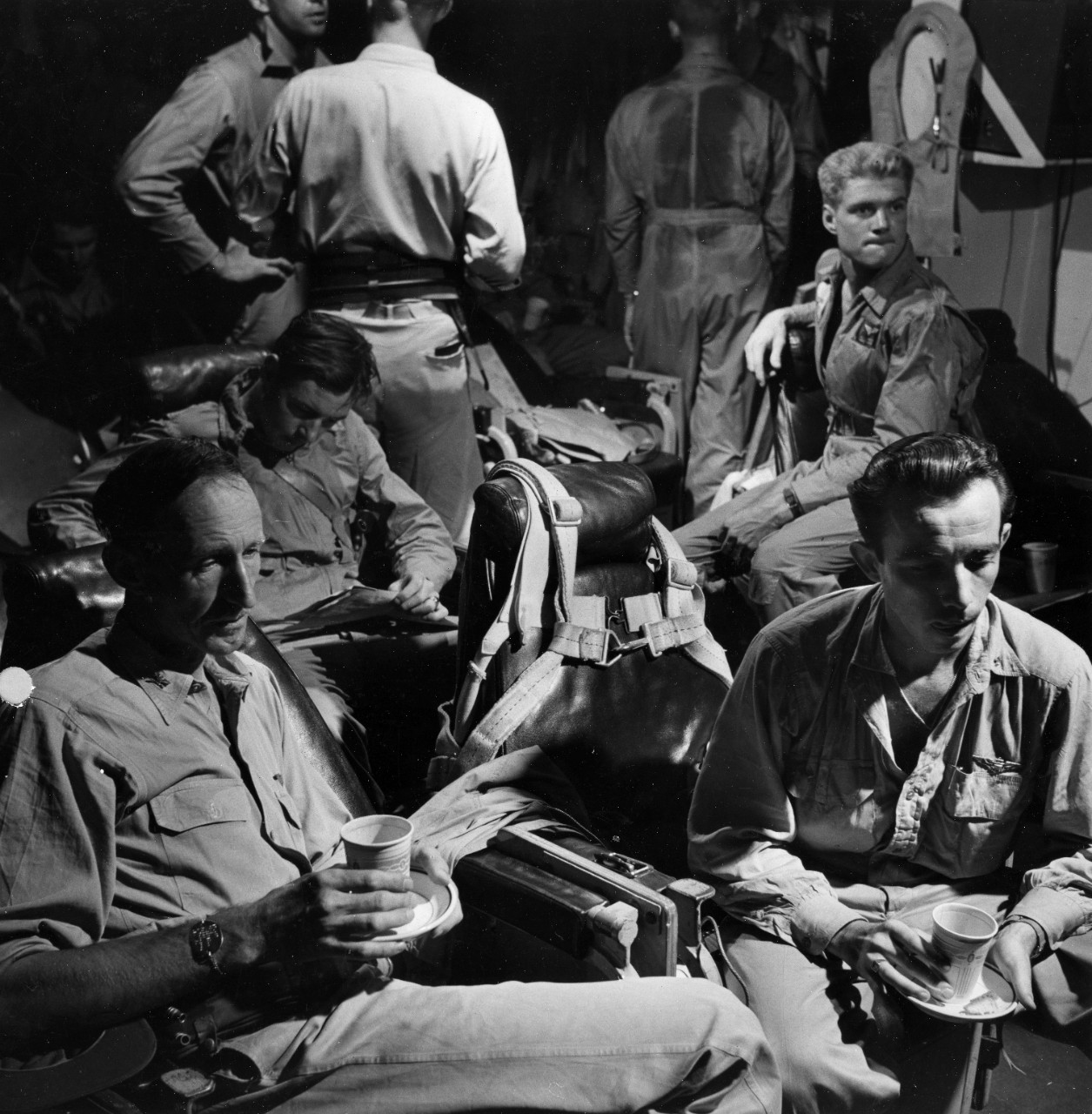 Tense scene in the pilots ready room of USS Monterey (CVL-26) as word is awaited from bombers about to attack Tinian, on 11 June 1944. Present are several fighter pilots who have just returned from an earlier strike on Gurguan Airfield, including ship's Air Group Commander, LCDR. Roger Mehle (seated, right front). With LCDR Mehle is the ship's CO, CAPT. Stuart H Ingersoll. 