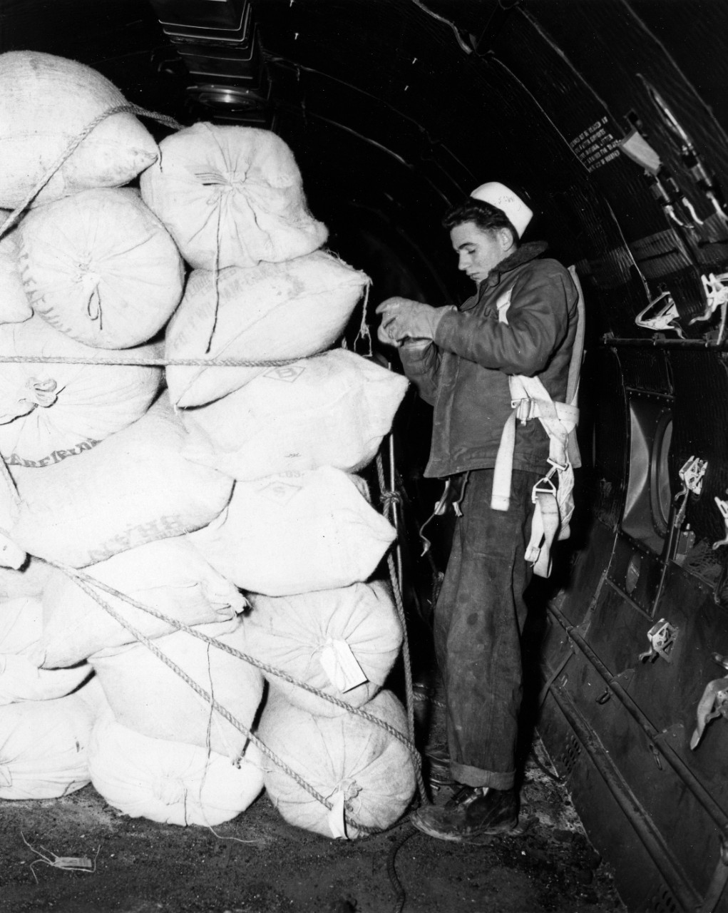 Airman Apprentice Robert H. Davidson is shown checking the lashings on the load of flour in his R5D (C-54).