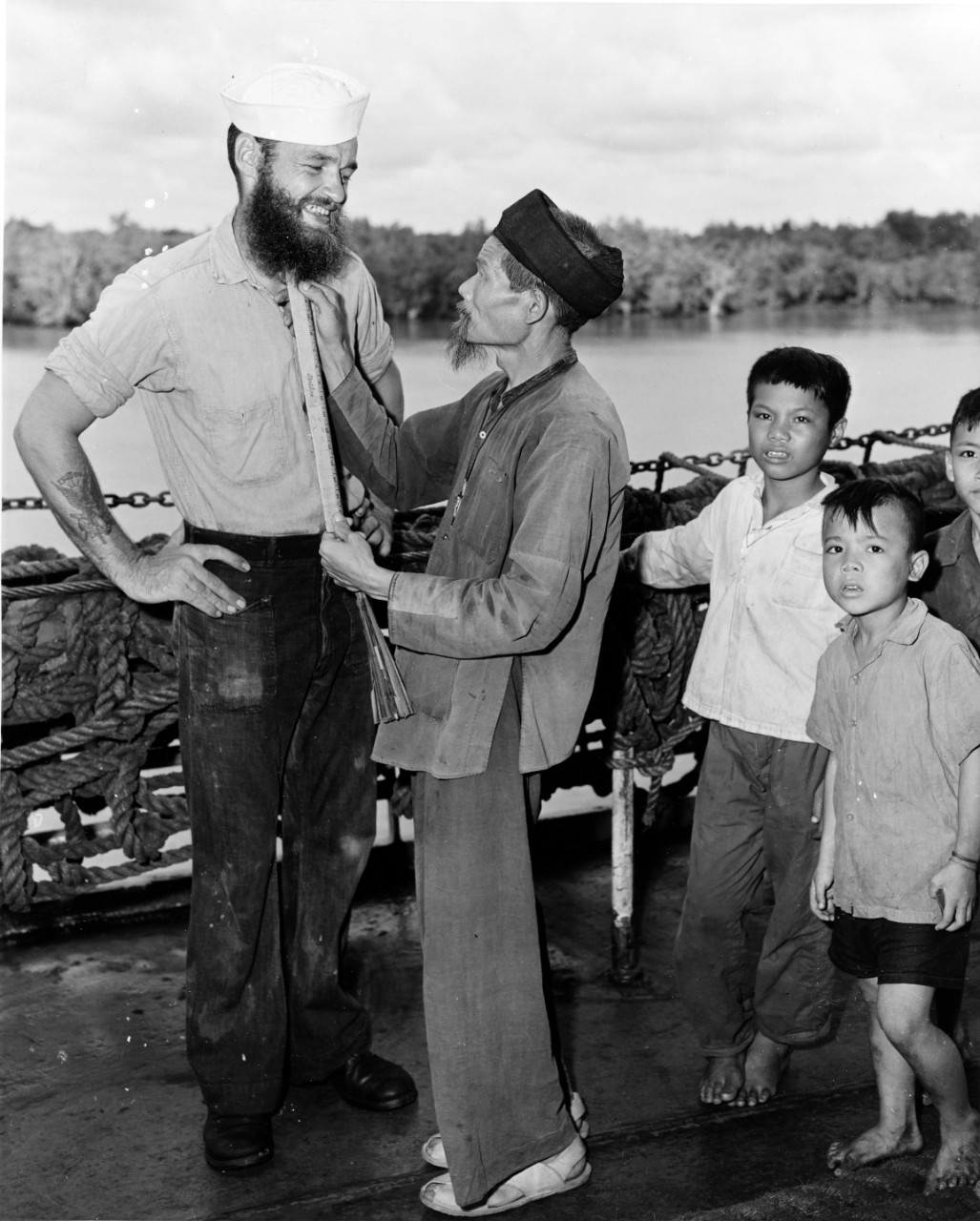 ENSN James I. Hart, USN, has his beard measured by a Vietnamese refugee white other refugees look on during their "Passage to Freedom" from Haiphong to Saigon, South Vietnam, 1954. 
