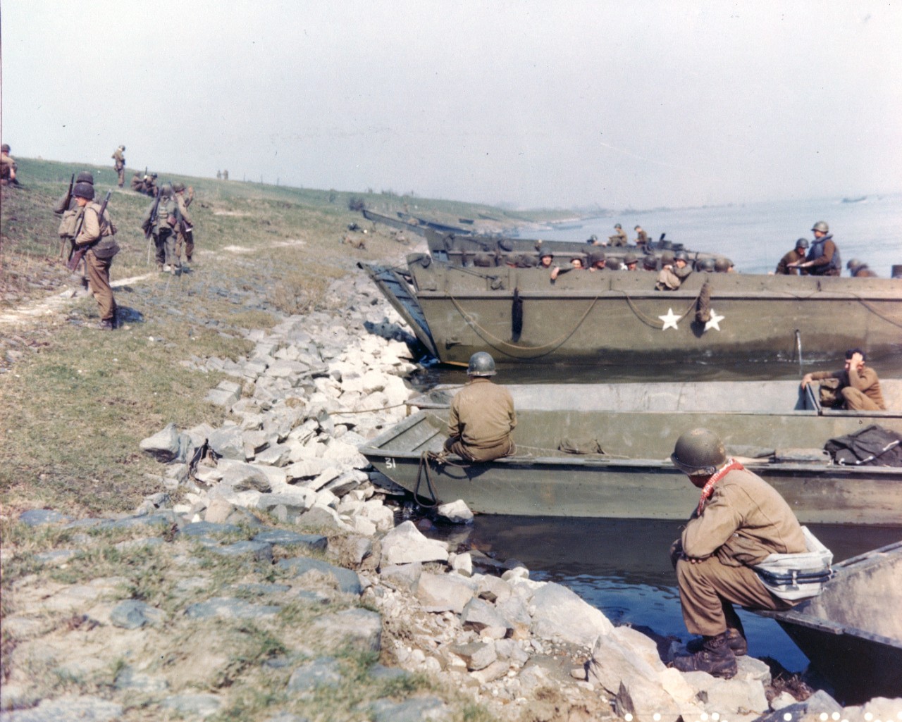 Men of the 1st Battalion, 314th Infantry Regiment, 79th Division, prepare to board LCVP landing craft, as the unit crossed the Rhine River at Orsoy, Germany, 10 March 1945. Boats in the foreground are Army bridge pontoons.