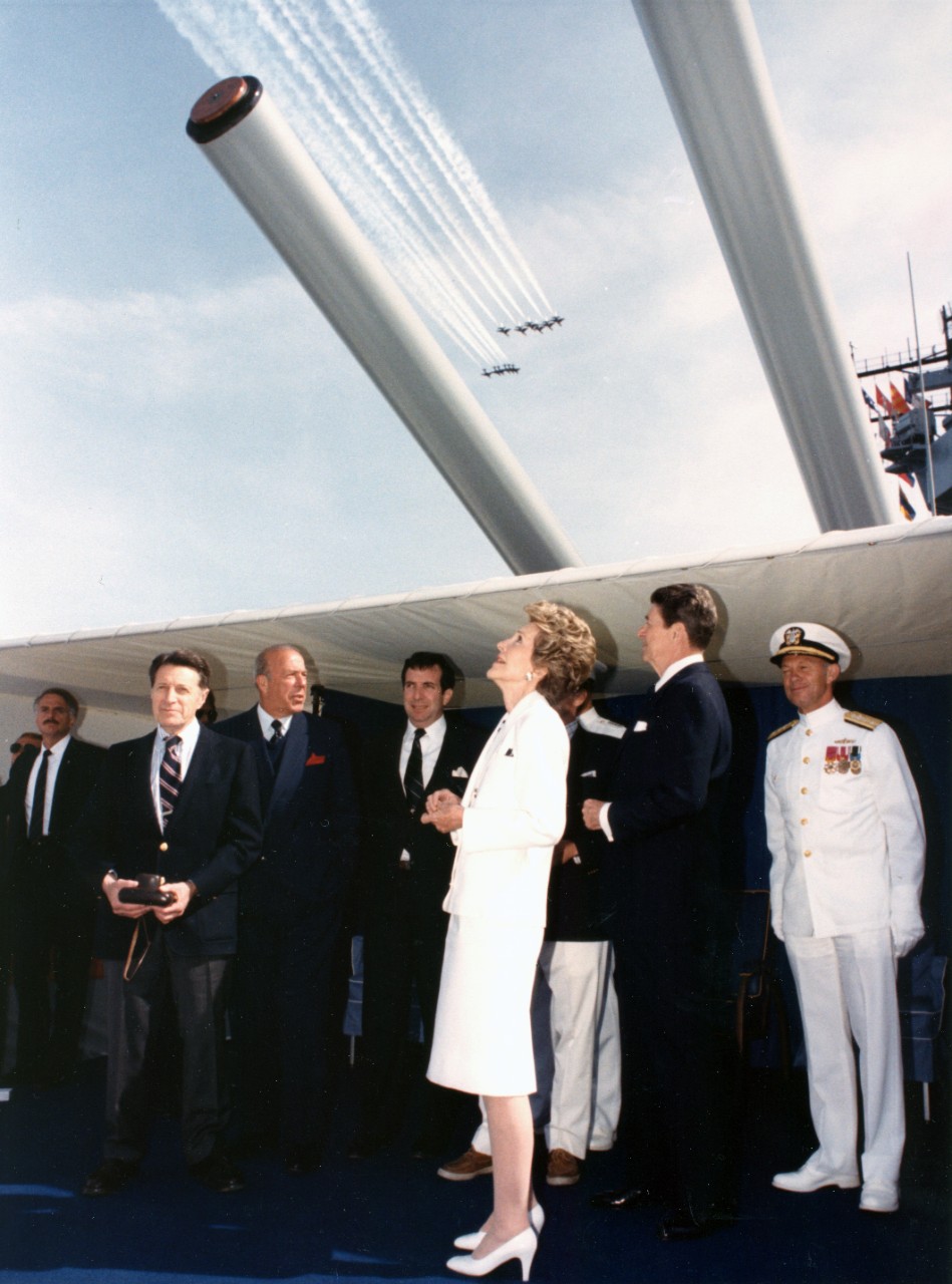President and Mrs. Ronald Reagan watch aircraft from the roof of Turret No. 1 on board the battleship USS Iowa (BB-61) during the International Naval Review. Also seen are Secretary of Defense Caspar Weinberger and Secretary of State George Shultz.