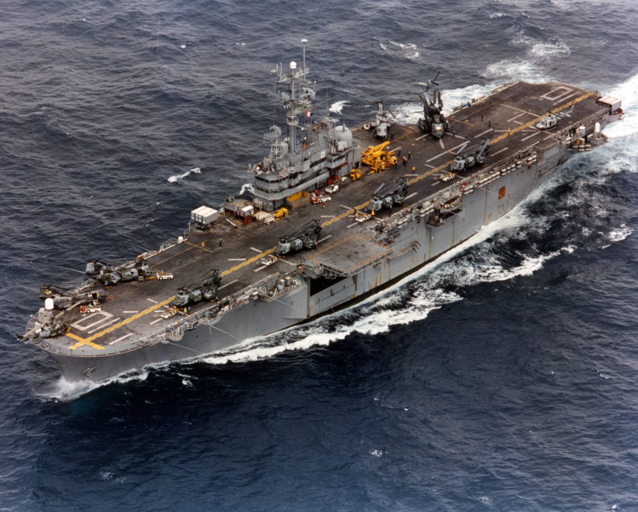 Aerial view of amphibious assault ship USS Tripoli (LPH-10) underway. There are a number of different helicopters on the flight deck, including MH-53E Seadragon, CH-46 Sea Knight, and Bell UH-1 types.