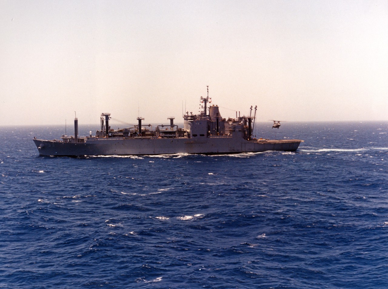 Port beam view of ammunition ship USS Shasta (AE-33) underway, circa March-July 1993. A CH-46 Sea Knight helicopter is operating over the ship's landing pad.