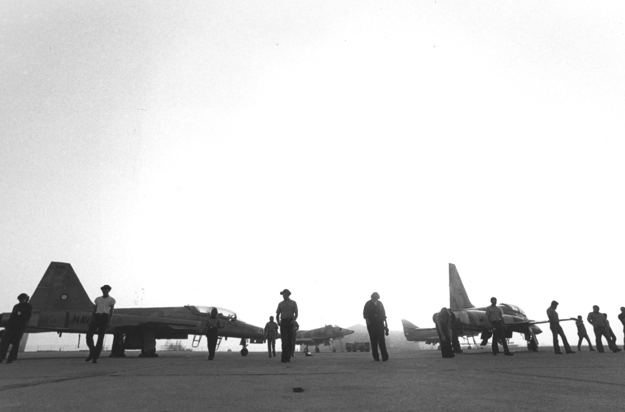 Maintenance crews walk onto a mist-covered flight line to prepare adversary aircraft of the Navy Fighter Weapons School at NAS Miramar, CA for an early morning flight. Known as "Top Gun," the school provides air combat maneuvering (ACM) training for Navy and Marine Corps pilots. Visible are two F-5F Tiger II aircraft and two A-4 Skyhawk aircraft (in background).