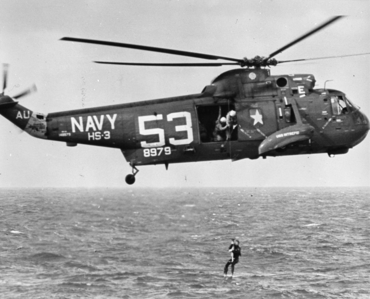 A frogman is lowered to the Gemini 3 spacecraft from a Navy helicopter of squadron HS-3. USS Intrepid (CV-11) was the prime carrier for the recovery operation for NASA's successful three orbit mission by Astronauts Grissom and Young.