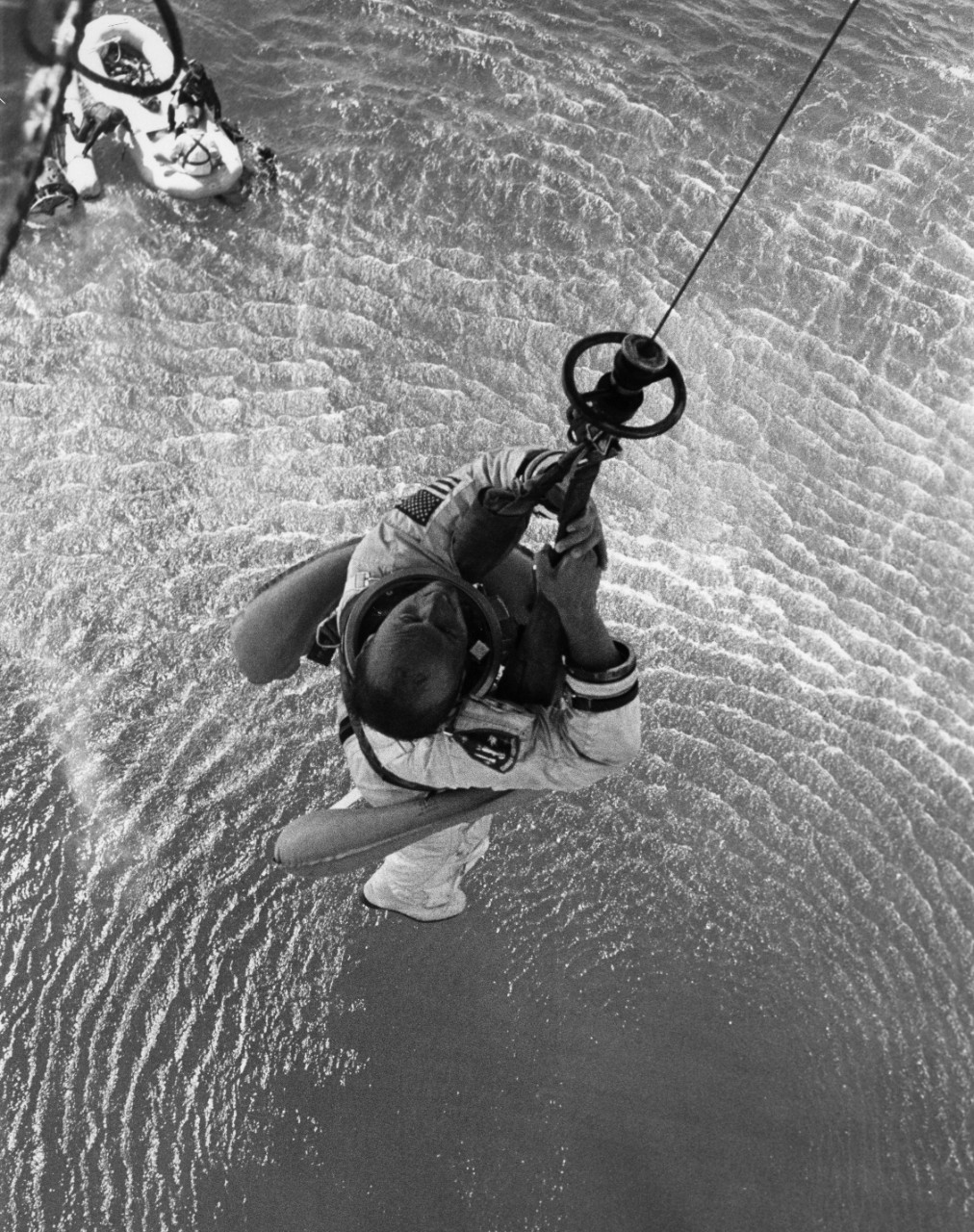 Gemini 11 astronaut Charles Conrad is hoisted aboard a recovery helicopter, with astronaut Richard Gordon in the raft below.
