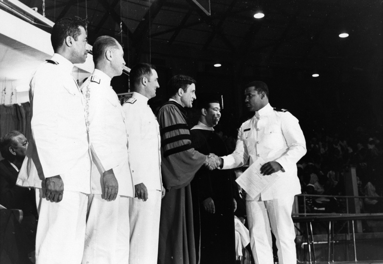 Secretary of the Navy John H. Chafee congratulates newly commissioned Ensign James Ealy from Palestine, Texas, after Ealy was sworn into the Navy following graduation with honors from Prairie View A & M College. Thirteen seniors were members of the first graduating class from the college in 1970.