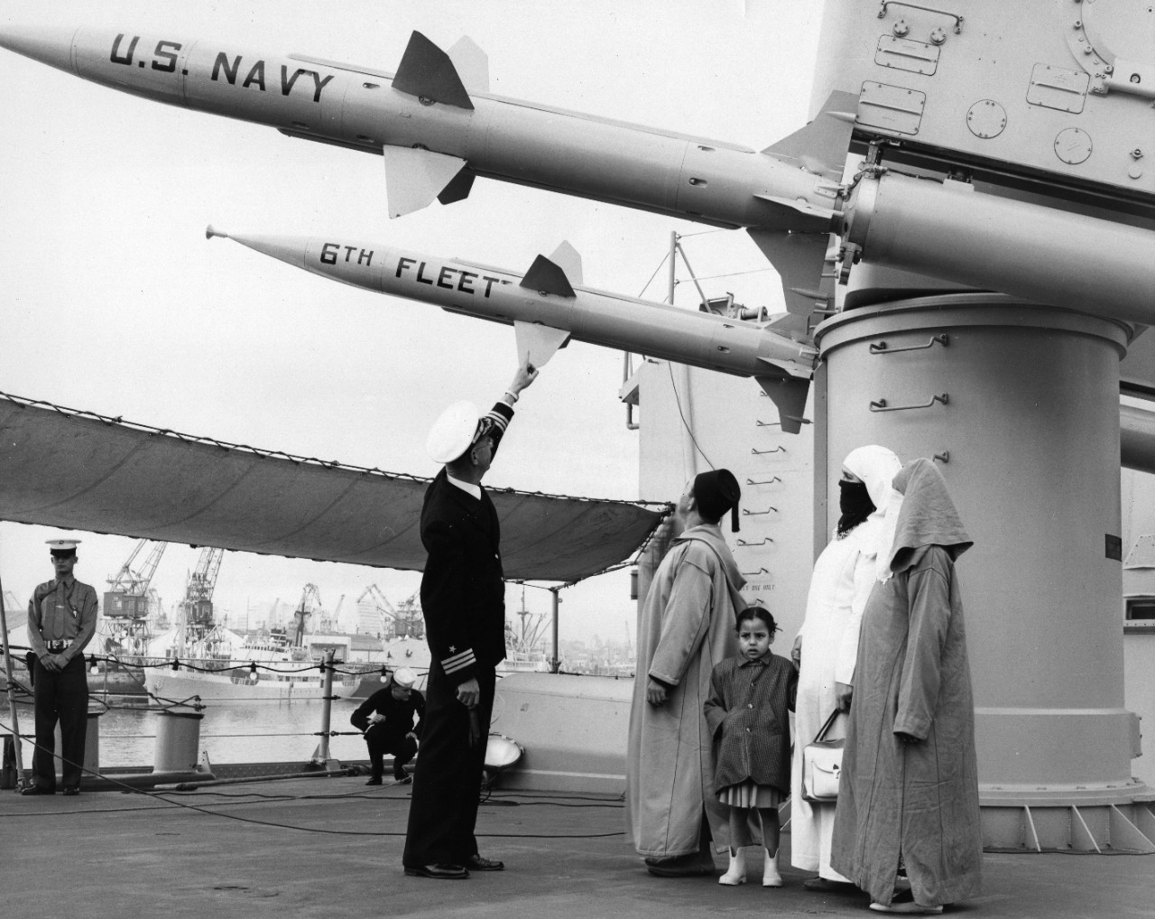 Modern missiles hang above Moroccans wearing traditional clothing, as Commander Travis O. Tabor III, Executive Officer of USS Springfield (CLG-7) explains the workings of the Terrier missile, during a Sixth Fleet visit to Casablanca.