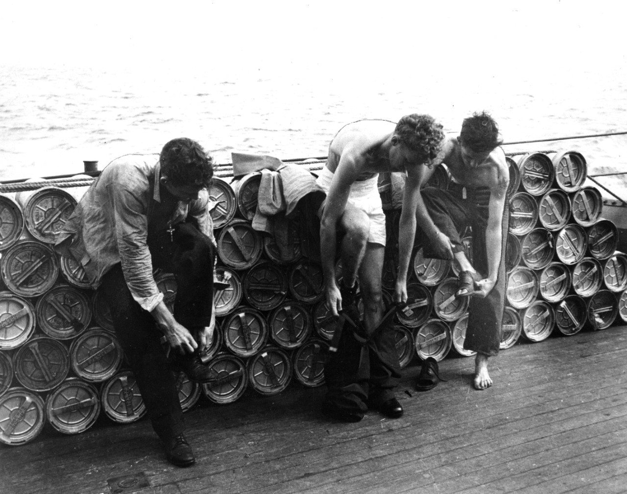 Given a new outfit of gear, survivors of the torpedoed USS Helena (CL-50) effect a change of ensemble aboard the warship which rescued them. They are (left to right) Fireman First Class Robert O. Dudley of Placerville, CA; Machinist's Mate Second Class Glenn B. Carlton of Huntington Park, CA; and Paul L. Benson of Council Bluffs, IA.