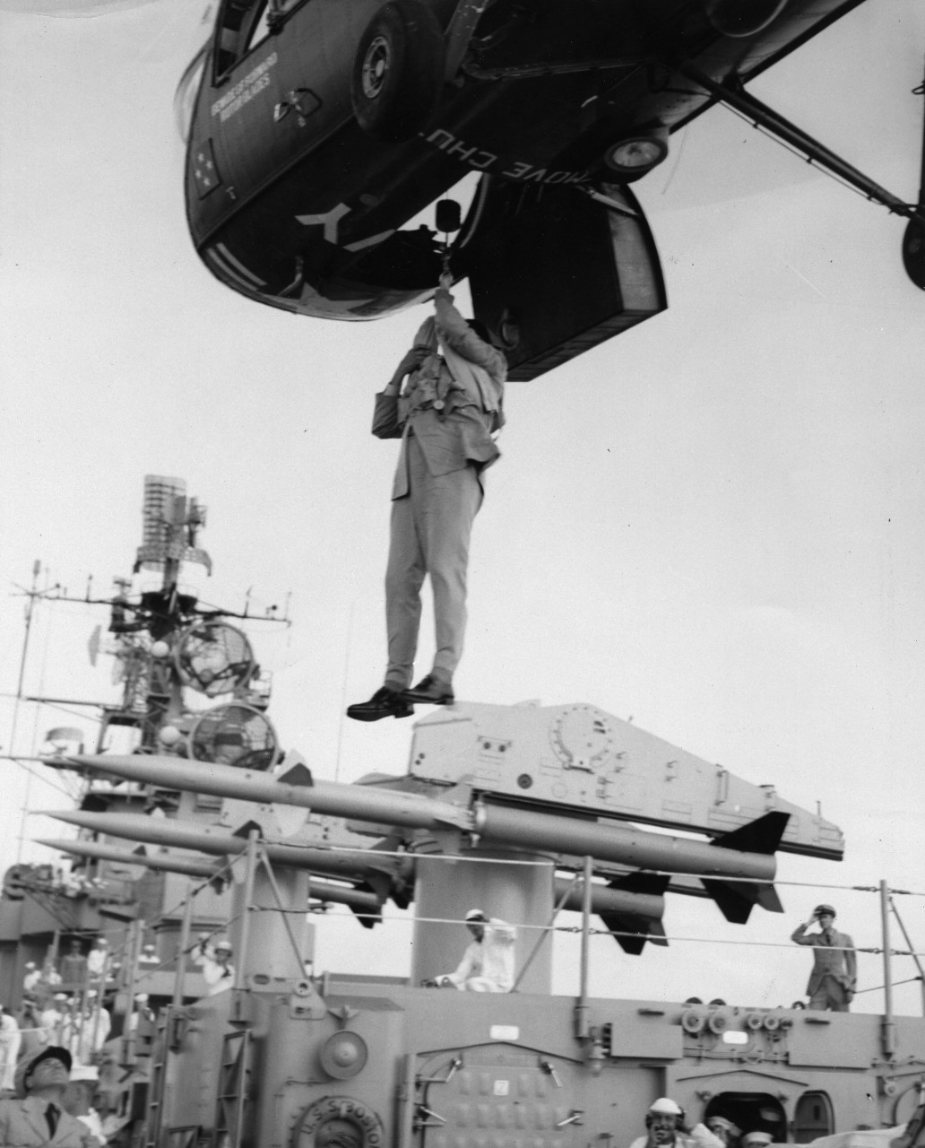 Unidentified officer on a hoist hanging from a helicopter, hovering above USS Boston (CAG-1)