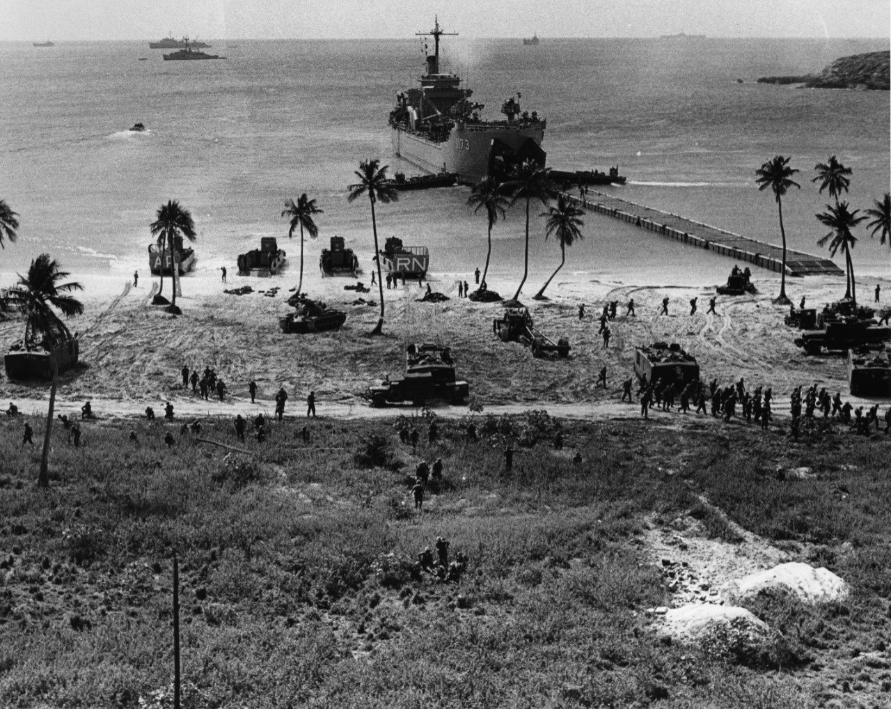 Tank landing ship USS Suffolk County (LST-1173), with the Second Fleet in the Caribbean, offloads tanks and vehicles, while US Marines storm ashore on the island of Vieques during LANTFLEX 66, a major Atlantic Fleet exercise. Other ships are visible in the background, as well as LCVP on shore.