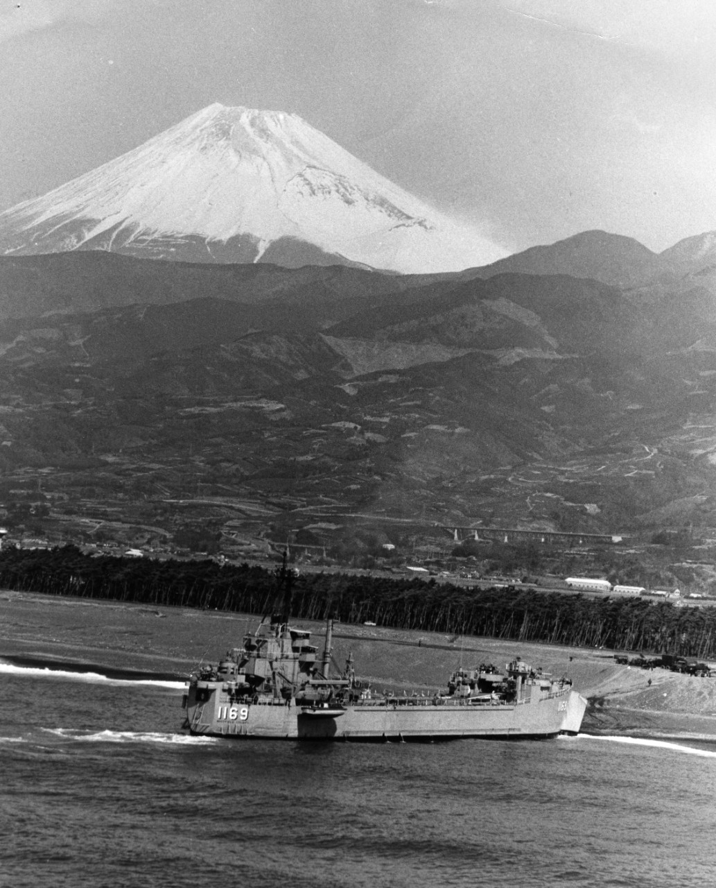 Tank landing ship USS Whitfield County (LST-1169) unloads elements of the Third Marine Division on the beach at Numazu, Japan. Snow-covered Mt. Fuji looms in the background.