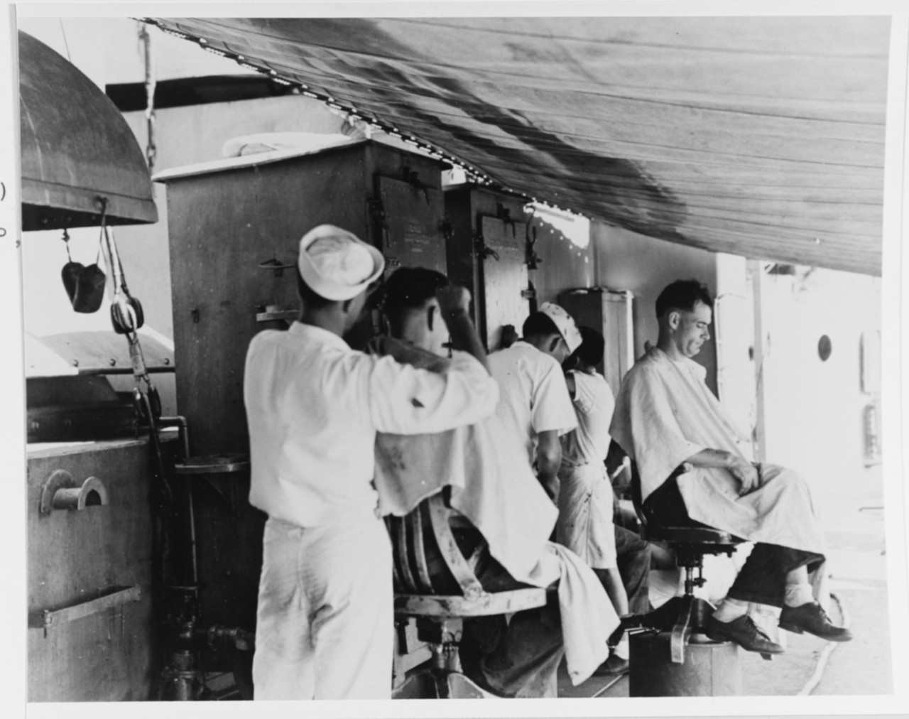 USS Marblehead (CL-12), view taken aboard ship in February 1942. Showing makeshift barbershop rigged up under an awning amidships. Shop belowdecks had been damaged during the air attack which heavily damaged the ship on 4 February 1942 in the Flores Sea.