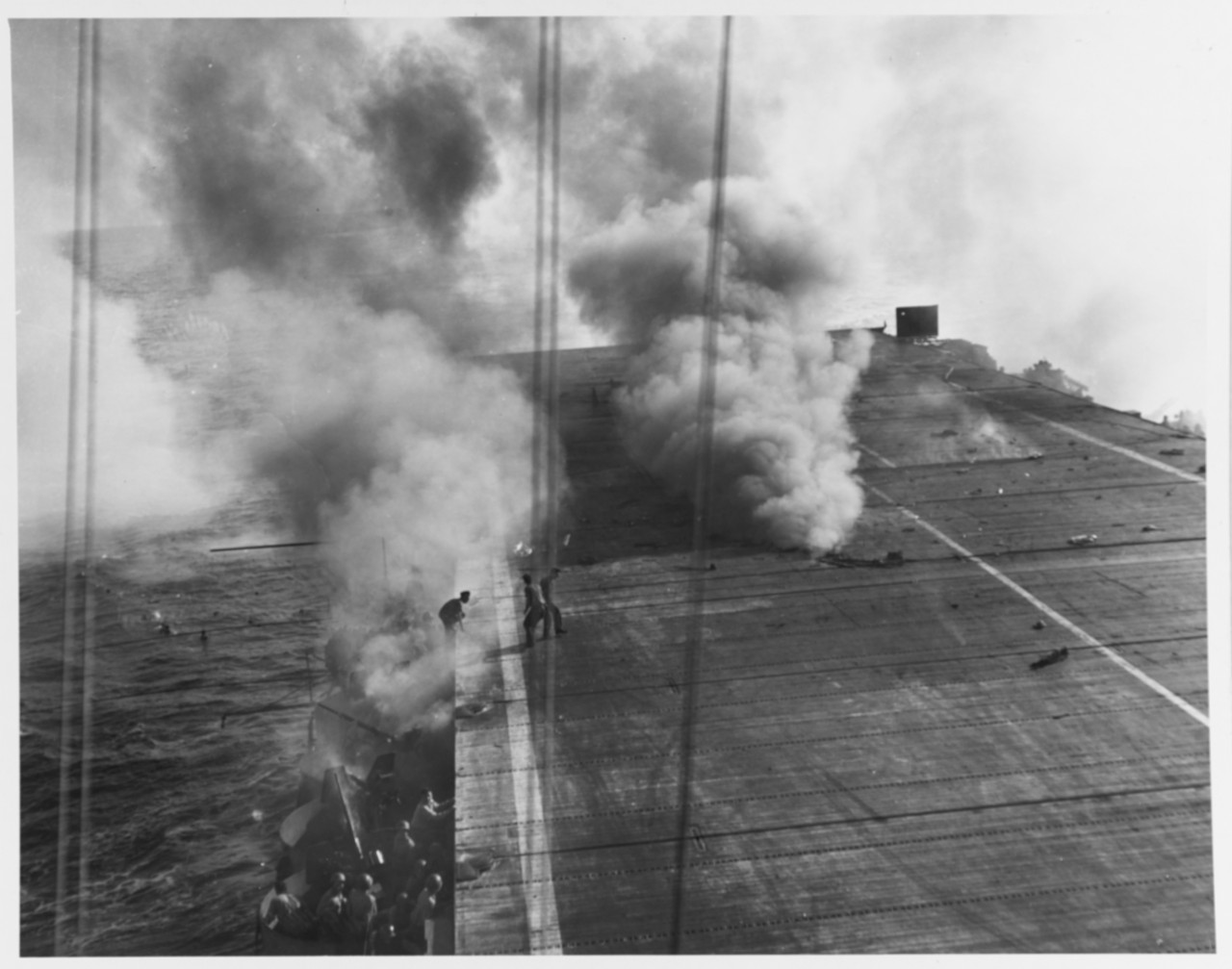 Crewman move from the galleries of USS Suwanee (CVE-27) to repair kamikaze damage to the after part of the flight deck, 25 October 1944. Smoke comes from fire in the hangar. Note men in the water.