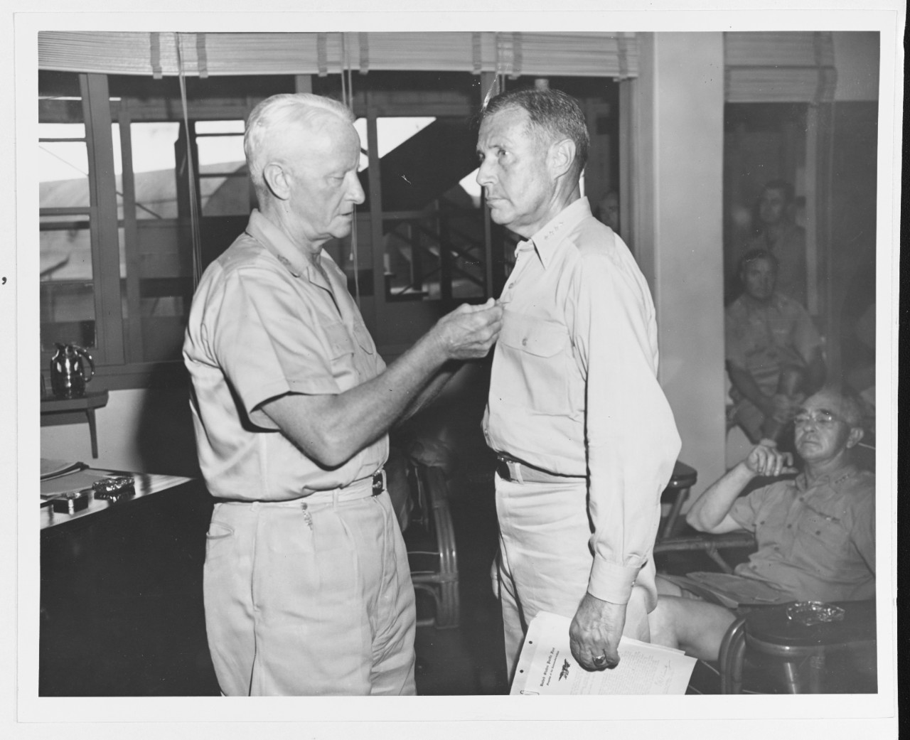 Admiral Raymond Spruance receives the Navy Cross from Fleet Admiral Chester Nimitz, at Pacific Fleet Headquarters, Guam, 1 June 1945. At right is Admiral Richmond K. Turner in hallway, at right in distance is Rear Admiral Forrest Sherman