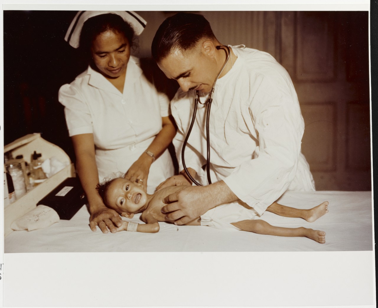 Lieutenant William B. Ruocco, USNR (MC) examines a baby in hospital at Agana, Guam, in 1944-1945