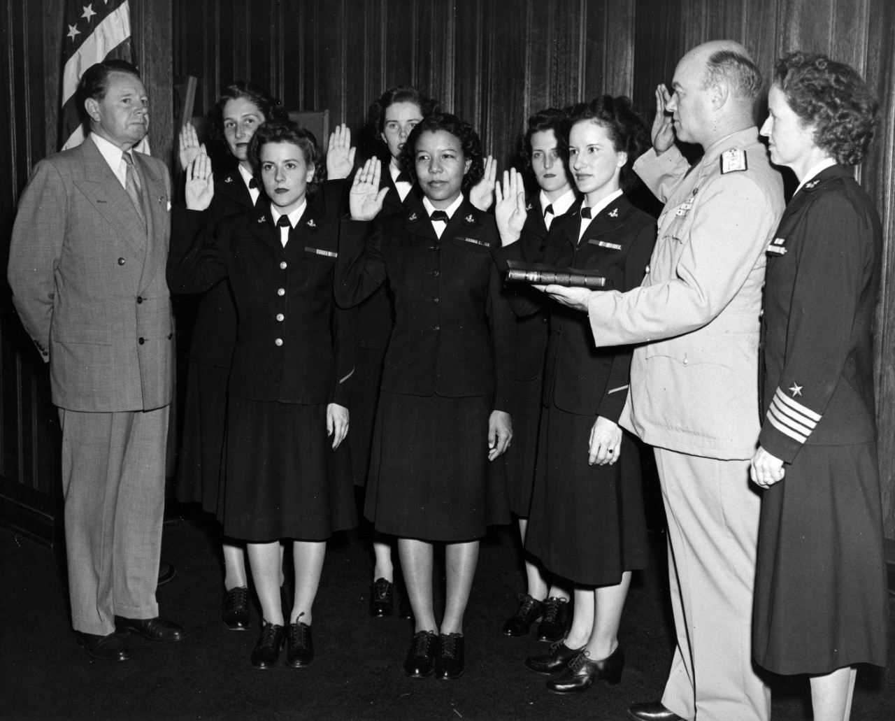 Swearing in of the first six women in the Regular Navy while the Secretary of the Navy John L. Sullivan, far left , looks on. Captain Joy B. Hancock, Director of the Woman's Reserve, is to RADM Russell's left, 7 July, 1948. The first six enlisted women are: (front row, left to right) Chief Yeoman Wilma J. Marchal, USN; Yeoman Second Class Edna E. Young, USN; and Hospital Corpsman First Class Ruth Flora, USN. Second Row (left to right): Aviation Storekeeper First Class Kay L. Langen, USN; Storekeeper Second Class Frances T. Devaney, USN; and Teleman Doris R. Robertson, USN. 