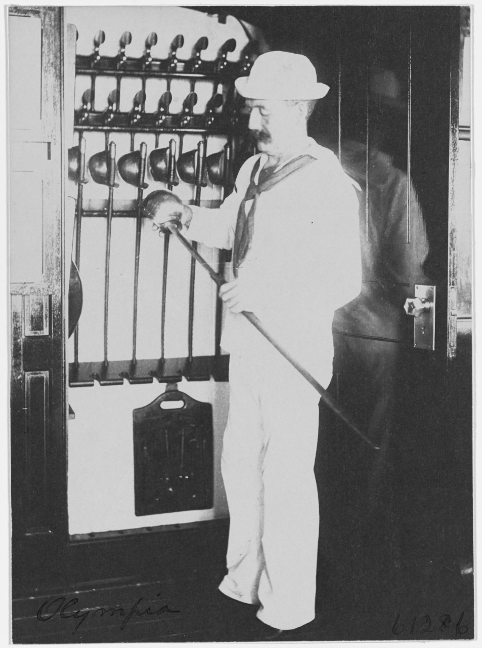 USS OLYMPIA (C-6), sailor poses with a rack of cutlasses and revolvers, 1898. 