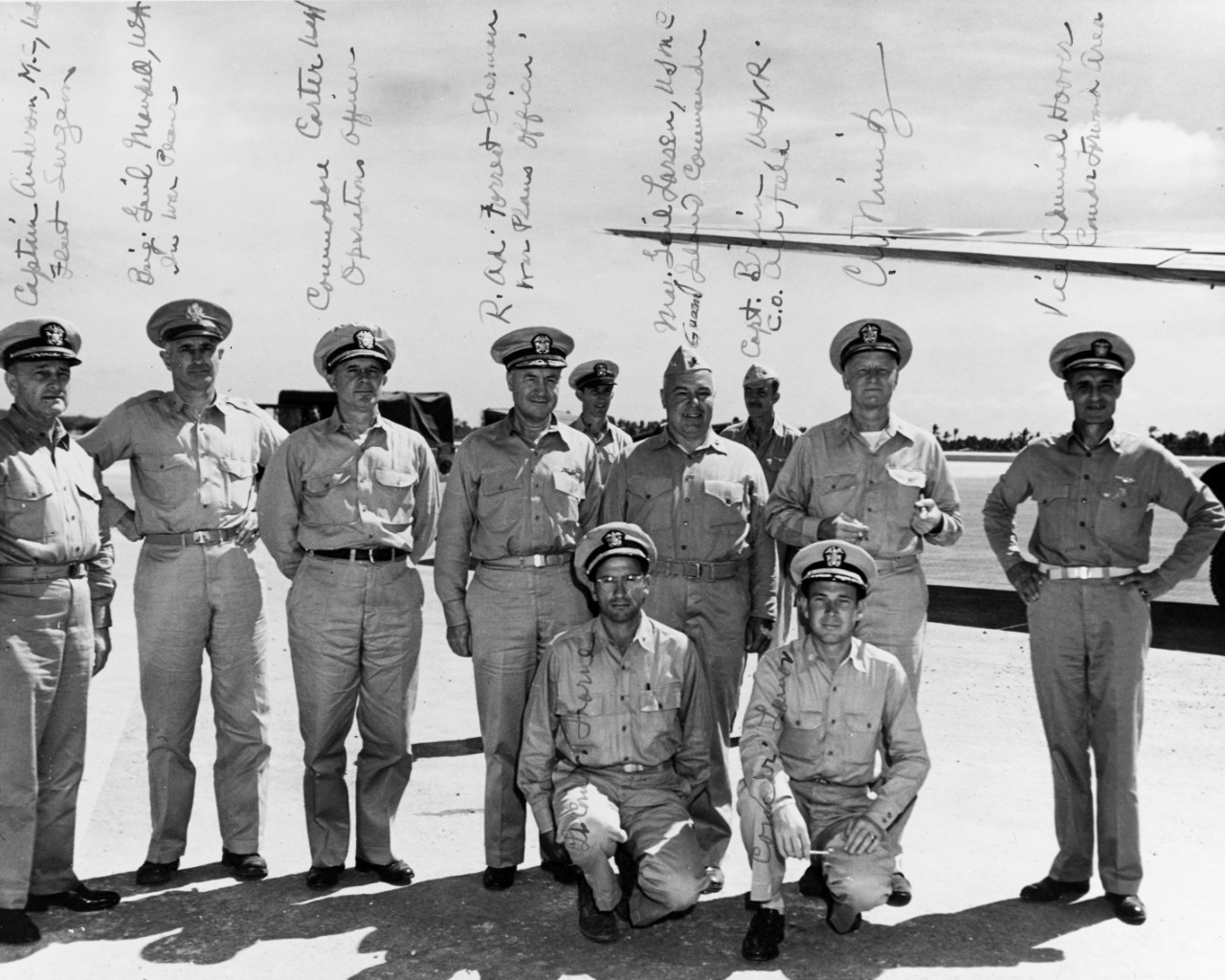 Fleet Admiral Chester W. Nimitz (CINCPAC-POA) arrives at his advanced headquarters at Guam, 27 January 1945, with part of his staff. L to R: Capt. T.C. Anderson (fleet surgeon); BGEN. H.C. Mandell, USA (war plans); COMMO. W.R. Carter, USN (Oper. Off.); RADM Forrest Sherman (war plans); UNIDENT. Off.; MGEN. N.L. Larsen, USMC (Guam Is. CDR.); CAPT. Brimm, USNR (C.O. Airfield Rear); FADM Nimitz; VADM J.H. Hoover, USN (CDR, Forward Area). Kneeling, L to R: LCDR. Horne and CDR. H.A. Lamar, USNR. The handwriting in FADM Nimitz's.