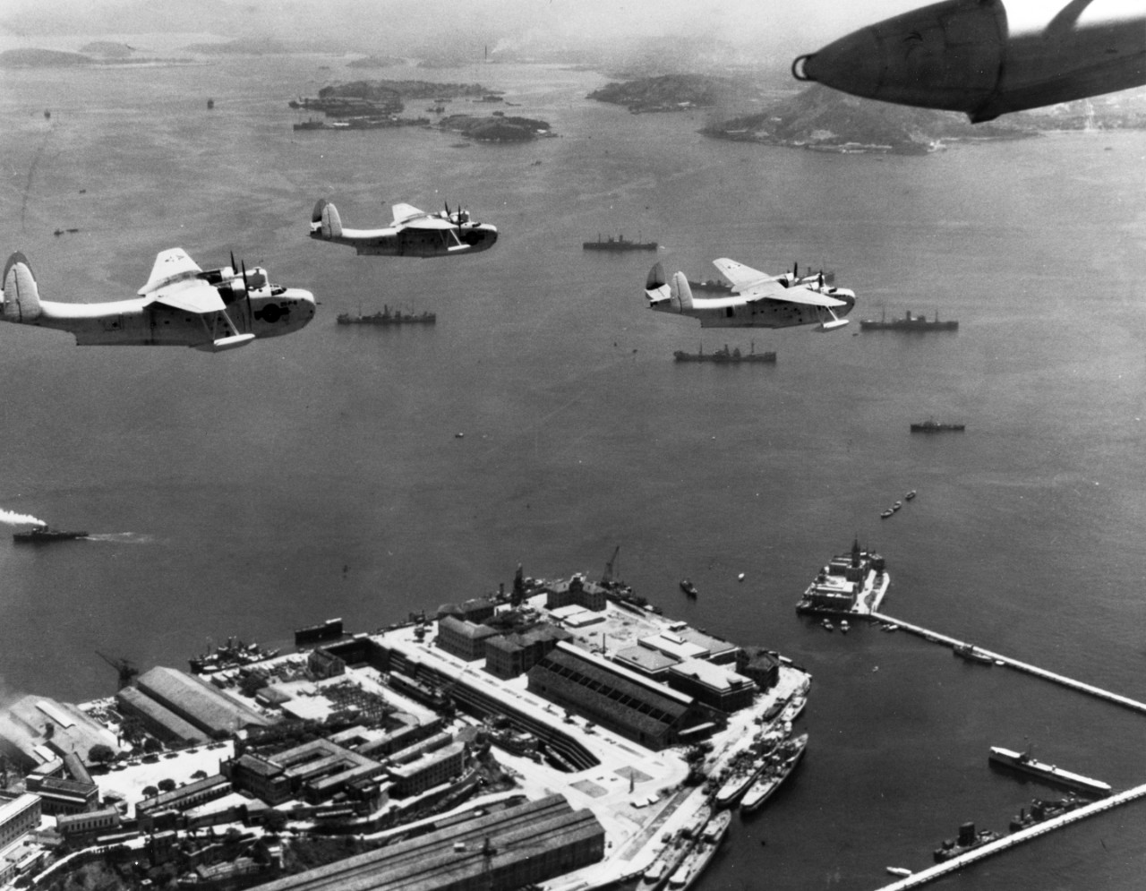 Martin PBM-3 Mariner Patrol Bombers of VP-211 fly in formation over the Brazilian naval dockyard at Rio de Janeiro, Brazil, December 1943. Several incomplete destroyers are among the ships at the yard. NARA photo number 80-G-56965.