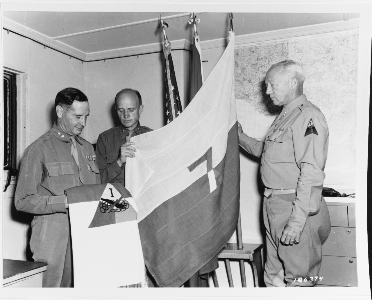 Sicily Invasion, July 1943. Major General Geoffrey Keyes, Brigadier General Hobart Gay, Lieutenant General George S. Patton, CG, 7th Army examining a 7th Army flag.