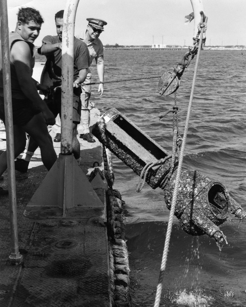 Binnacle from SMS Cormoran is hauled out of the waters of Guam Harbor, 1965. Officer at rear may be Captain W.L. Marshall, Commanding Officer of the Ship Repair Facility.
