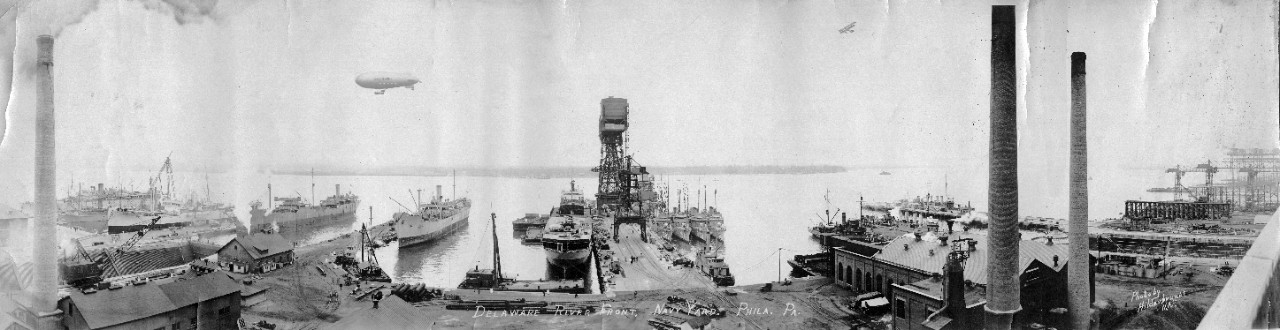 Waterfront, Philadelphia Navy Yard, PA, looking out into the Delaware River, ca. 1921. Visible ships include (left to right): USS Wright (AV-1), USS Fulton (AS-1), USS Gold Star (AK-12), USS Kaweah (AO-15), USS Yukon (AF-9), USS Dobbin (AD-3), USS Simpson (DD-221), USS Ellis (DD-154), USS MacLeish (DD-220), USS Blakeley (DD-150), and USS Cormorant (AM-40). U.S. Army blimp D-4 is airborne over the Delaware River in the background.