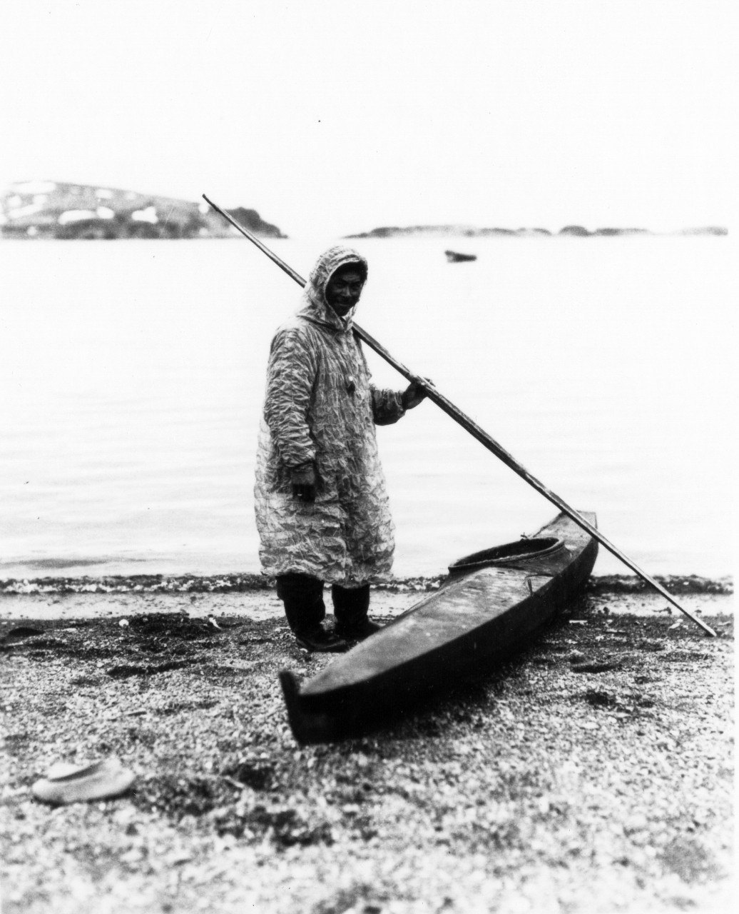<p>UA 437.04.012 A native of the Aleutian Islands dressed in a &quot;Kamelika&quot; with a &quot;Bidarka&quot; or skin boat. In these frail craft the Aleutians have for centures navigated through the islands, even in winter.</p>
